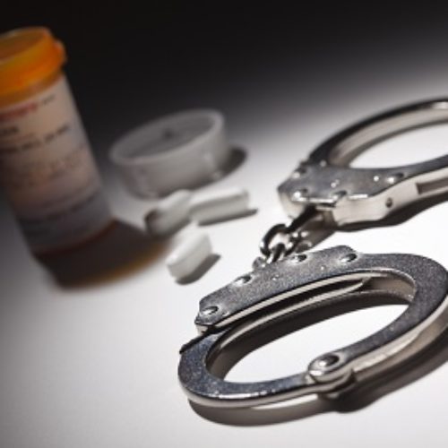 Handcuffs, Medicine Bottle and Pills Under Spot Light Abstract.